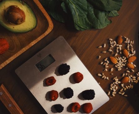 Top view of composed raw almond with seeds and avocado on table with berries on scales for cooking healthy dish